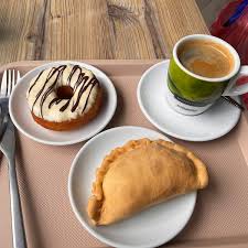 Una dona glaseada y una empanada junto a una taza de café